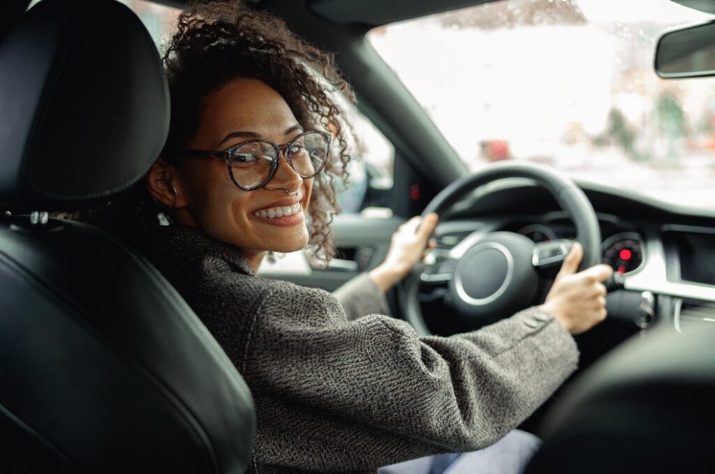 Smiling woman manager driving car and holding both hands on steering wheel on the way to work
